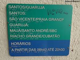 Placa informativa sobre linhas e horários de ônibus com escrita a tinta e em Braille